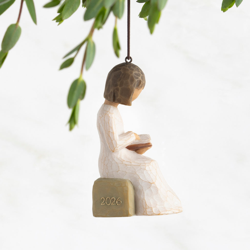 Profile view: Ornament of seated figure reading a book; 2026 in raised gold numbers on rock; loop and hook in head