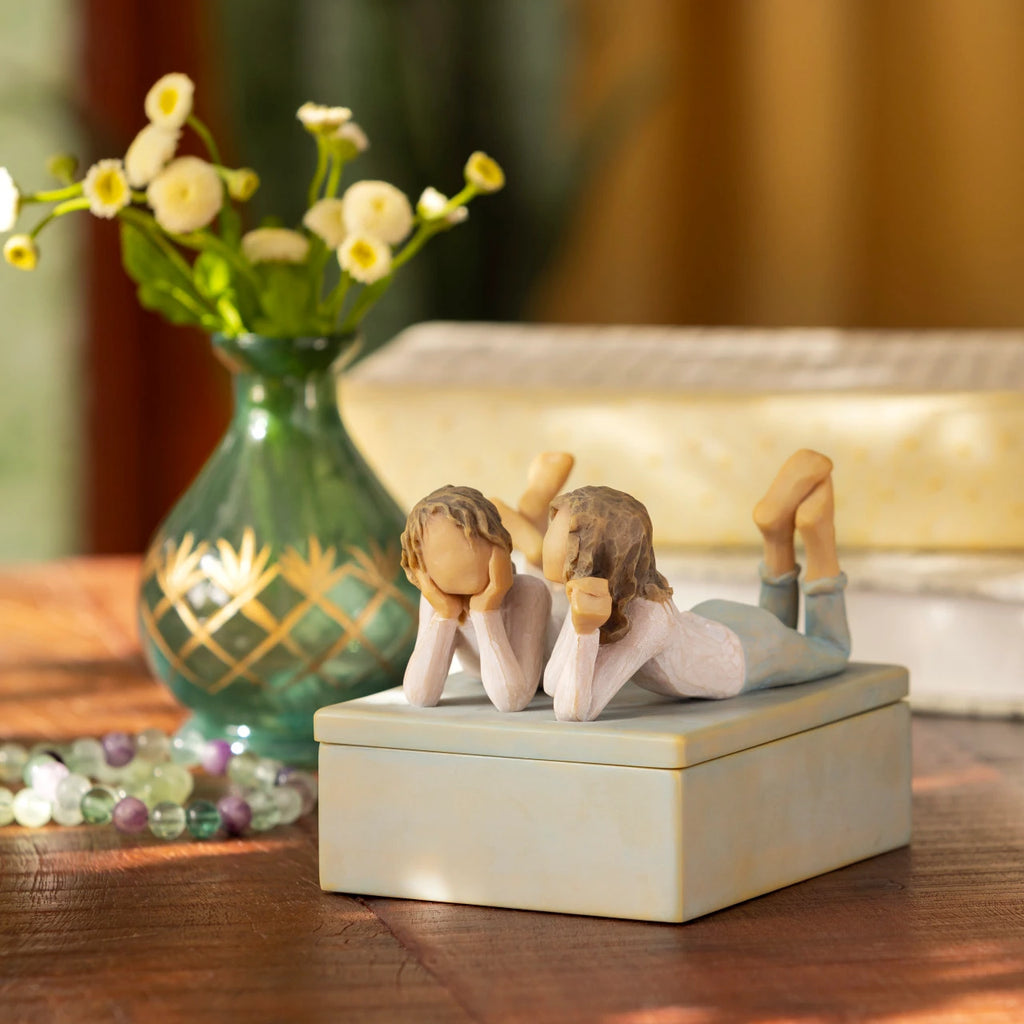 Willow Tree Forever Friends Keepsake Box, 4.25”d x 3.5”w x 3.75”h hand-painted blue-gray rectangular resin box, sculpture of two girls lying next to each other affixed to lid, on wooden table